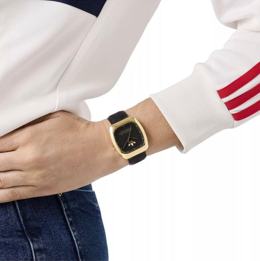 Adidas AOSY24528 watch worn on a wrist beside a white sleeve with red stripes.