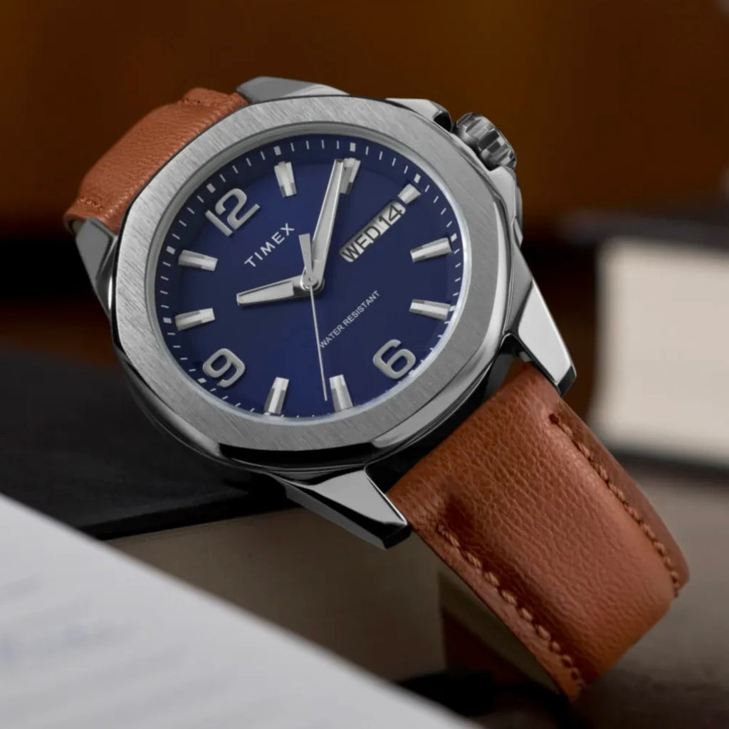 Timex Mens Watch Essex Avenue TW2W92800, blue dial, silver case, brown leather strap, resting on a brown surface at a slight angle.