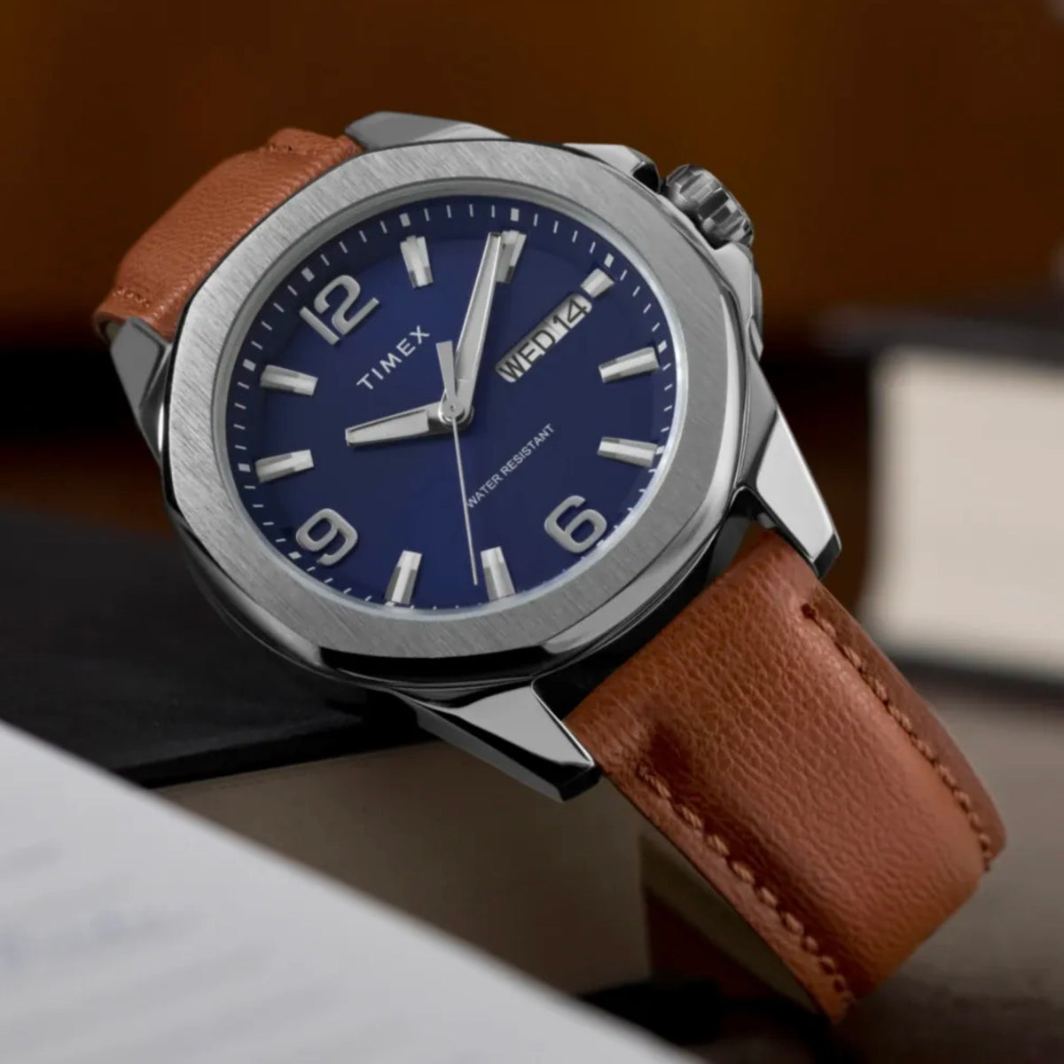 Timex Mens Watch Essex Avenue TW2W92800, blue dial, silver case, brown leather strap, resting on a brown surface at a slight angle.